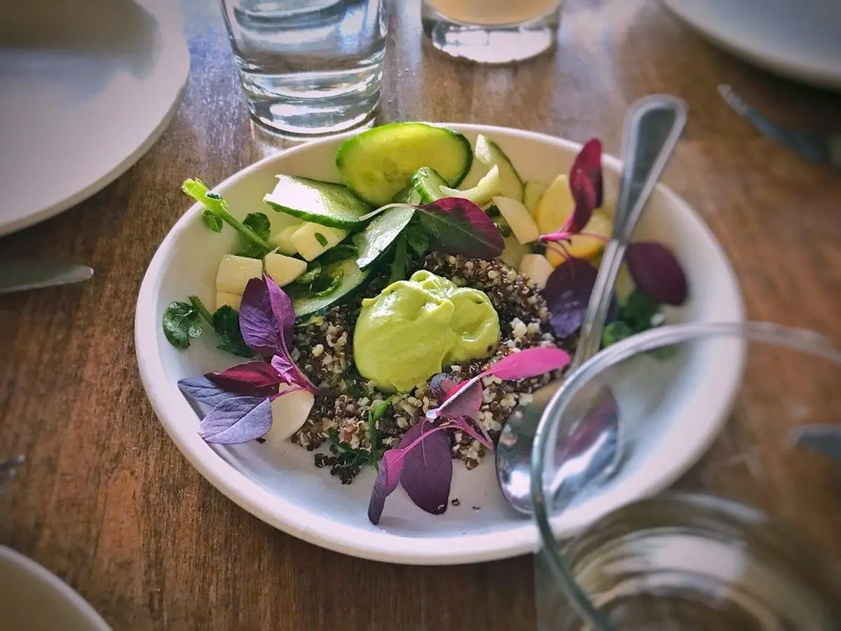 Cuenco de quinoa con aguacate, flores comestibles y hojas verdes sobre una mesa de madera