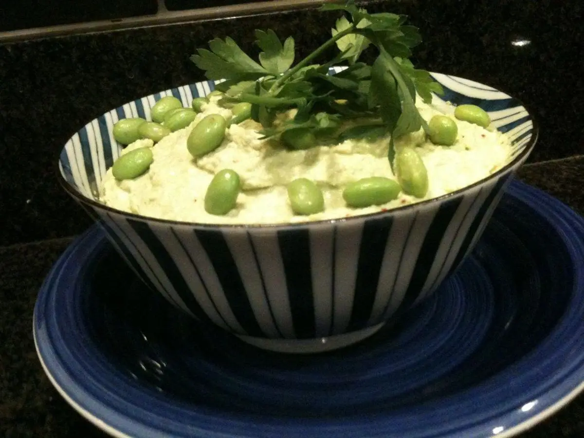 Cuenco de crema verde suave con edamame y hojas frescas por encima sobre un plato azul