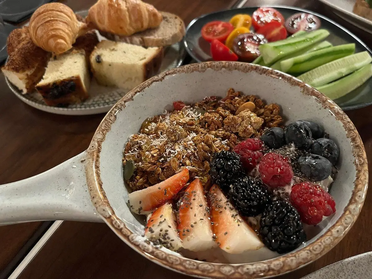 Bol de yogur con granola, frambuesas, moras y rodajas de fresa sobre una mesa de desayuno