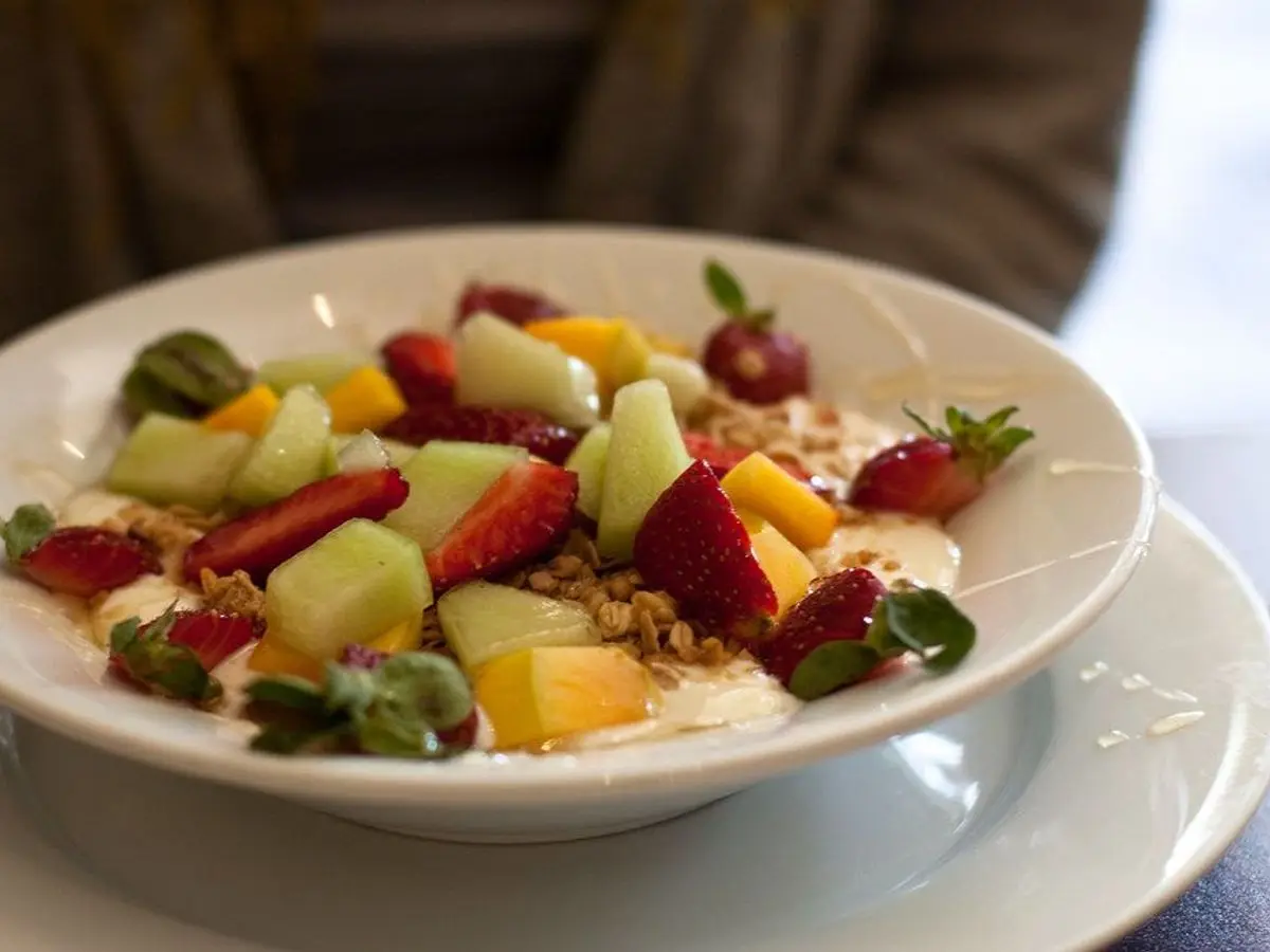 Plato de yogur con trozos de mango, kiwi, fresas y uvas por encima