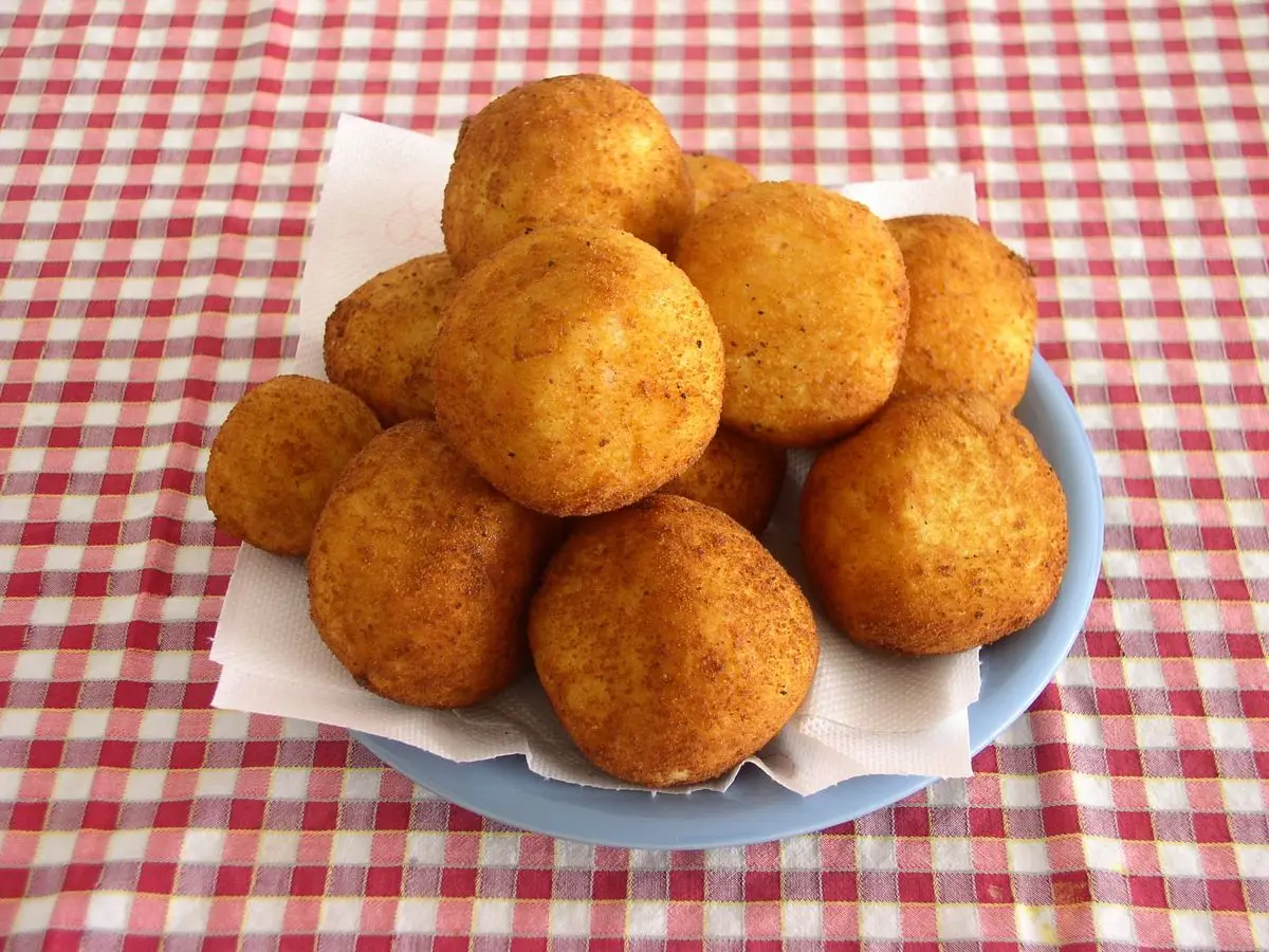 Croquetas de arroz doradas amontonadas en un plato sobre un mantel de cuadros rojos