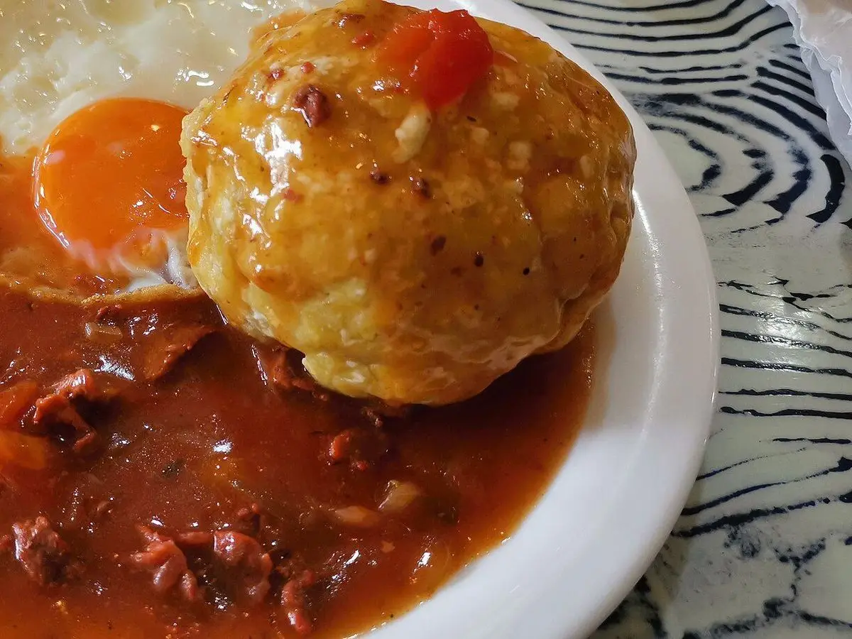 Bolón de plátano verde junto a un huevo frito y salsa roja en un plato blanco