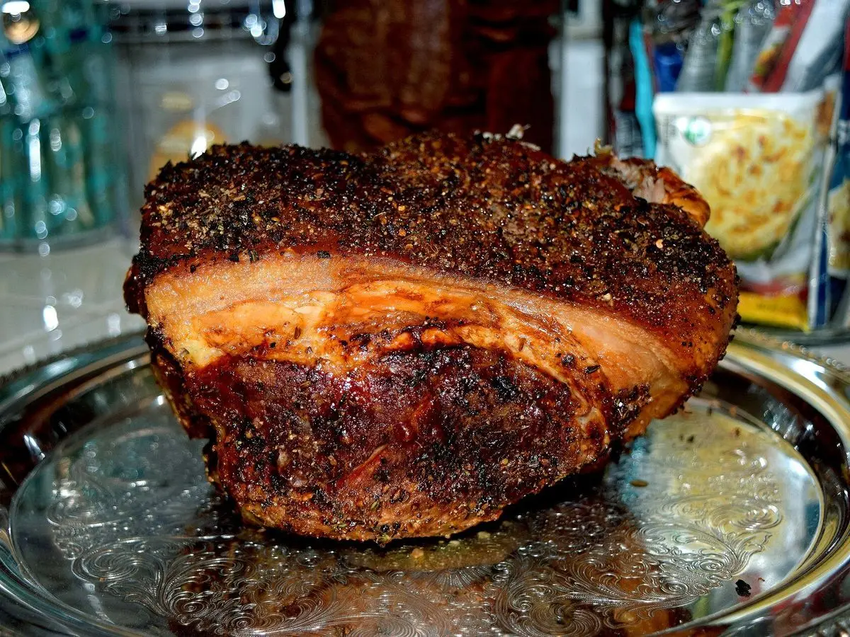 Paleta de cerdo asada con corteza dorada y especias sobre una bandeja plateada