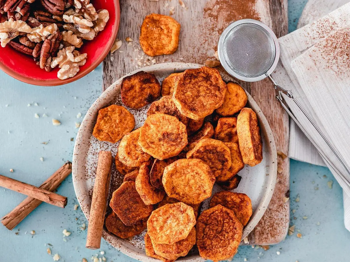 Rodajas de boniato asado con ramas de canela y nueces sobre una tabla de madera