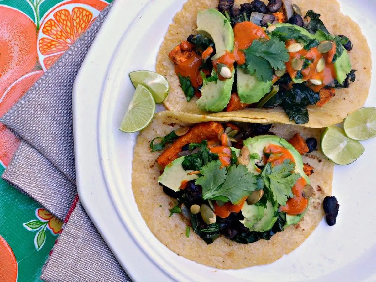 Dos tacos de boniato y alubias negras con aguacate, kale y rodajas de lima en un plato blanco