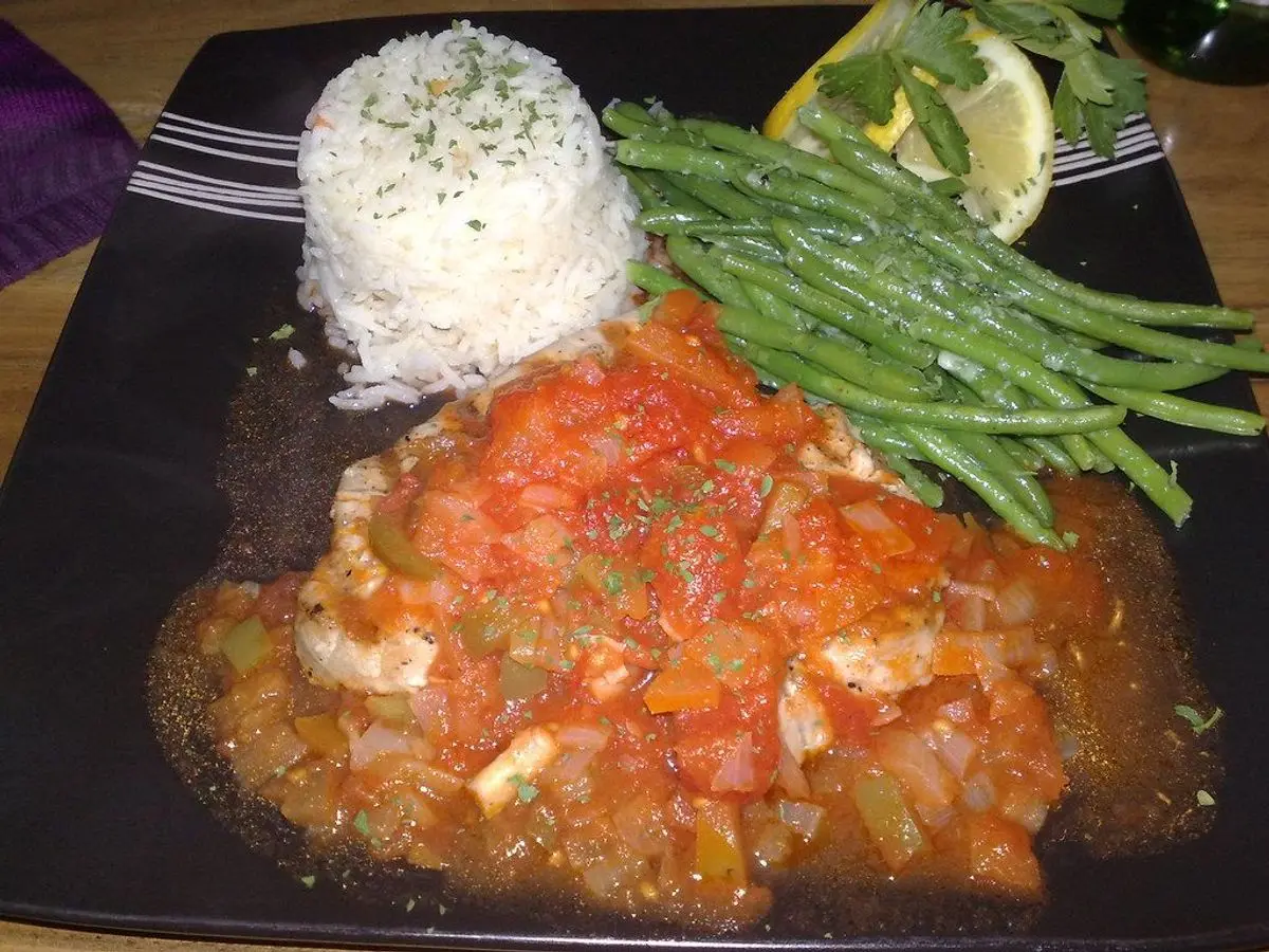 Pescado en salsa de tomate con arroz blanco y judías verdes en un plato oscuro