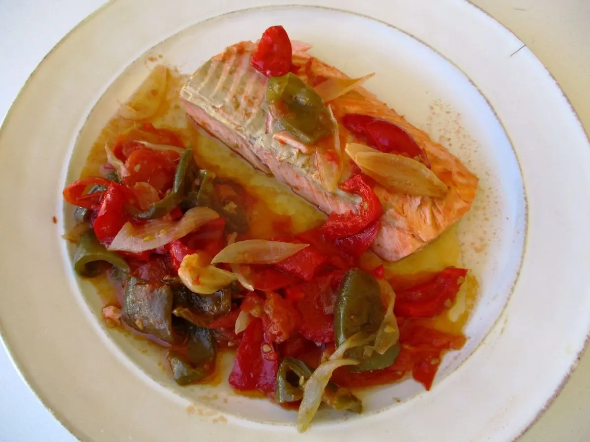 Pescado con pimientos y tomate estofados al estilo piperrada en un plato blanco