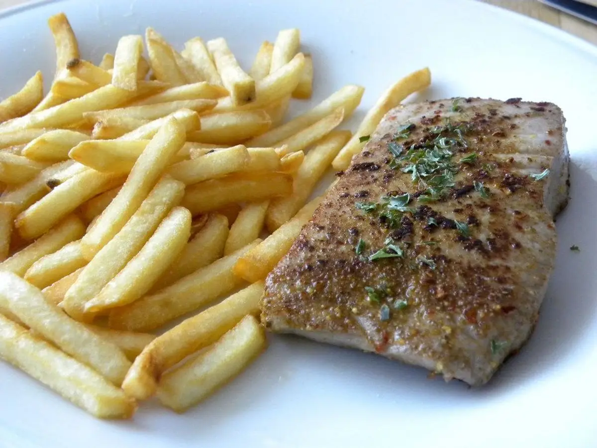 Filete de atún a la plancha con hierbas junto a patatas fritas en un plato blanco