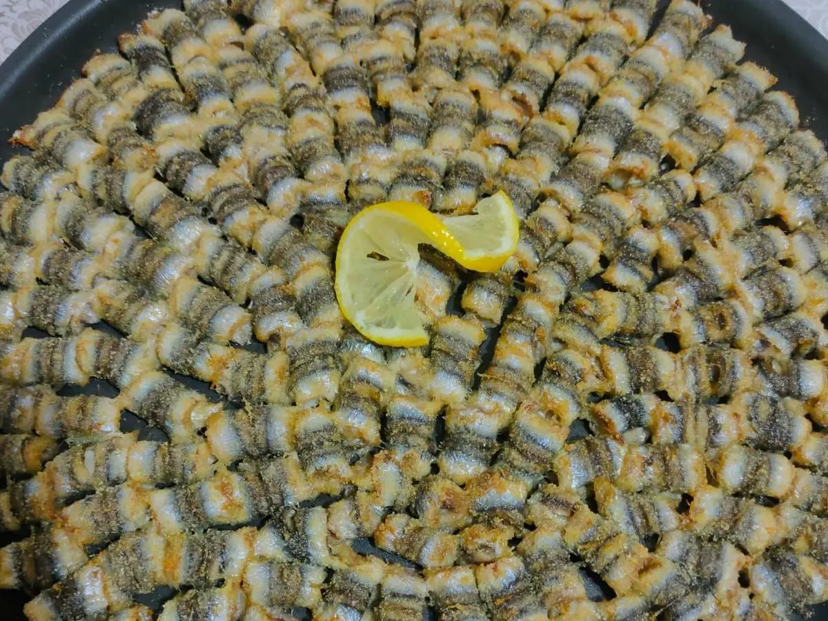 Boquerones al horno colocados en espiral en una fuente, con una rodaja de limón en el centro