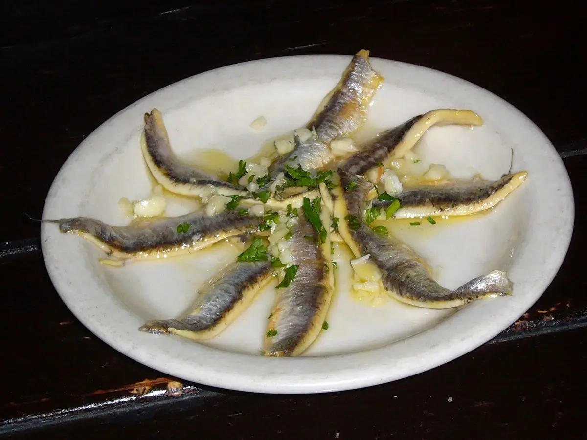 Plato blanco con boquerones marinados dispuestos en círculo con ajo y perejil