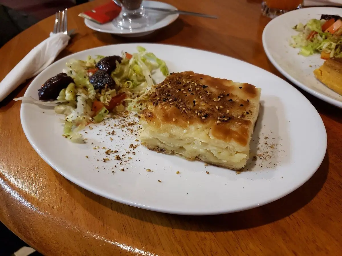 Porción cuadrada de börek de hojaldre filo dorado con una ensalada verde en un plato blanco