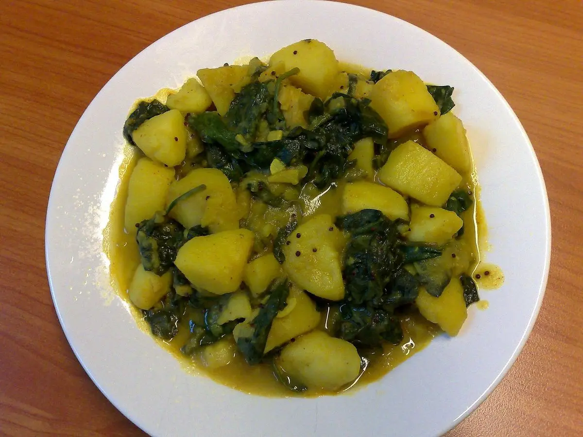 Plato blanco de dados de patata guisados con espinacas en un caldo especiado