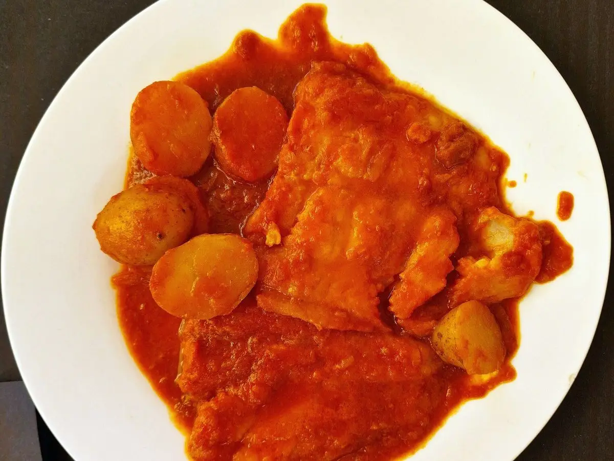Pescado en salsa roja picante con patatas pequeñas en un plato blanco