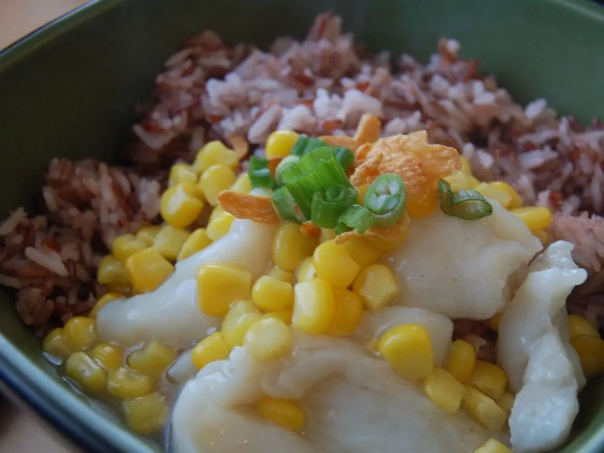 Cuenco verde de arroz integral con maíz y trozos de pescado blanco por encima
