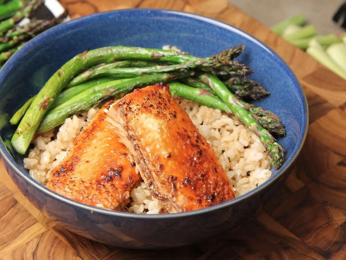 Bol azul con arroz integral, dos trozos de salmón glaseado y espárragos verdes asados