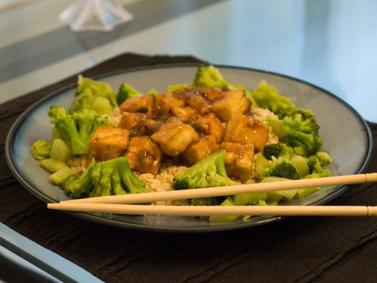 Dados de tofu glaseado sobre arroz integral con brócoli y unos palillos sobre el plato