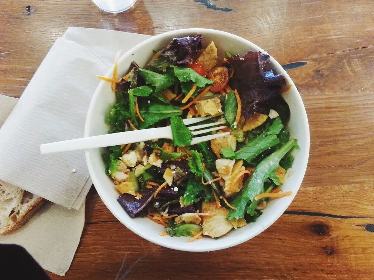 Cuenco con ensalada de hojas verdes, judías verdes y trozos de pollo sobre una mesa de madera