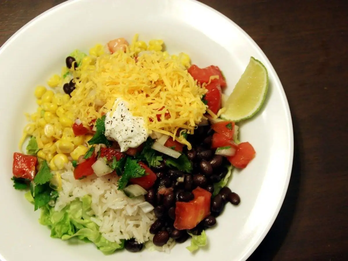 Plato blanco con arroz, alubias negras, maíz, tomate picado, lechuga y una rodaja de lima