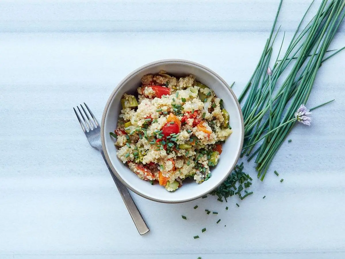 Cuenco de quinoa con verduras picadas y cebollino fresco junto a un tenedor