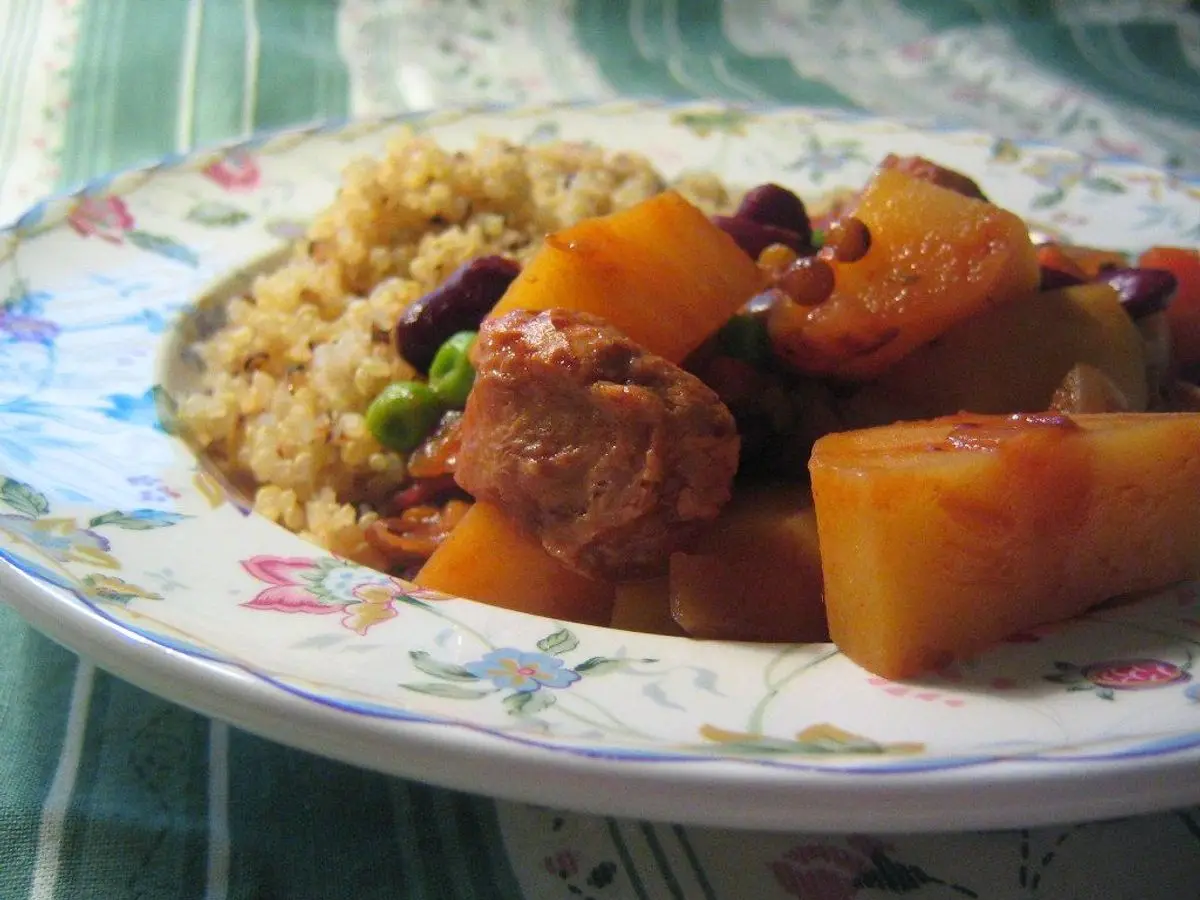 Plato con guiso de calabaza, guisantes y carne sobre quinoa