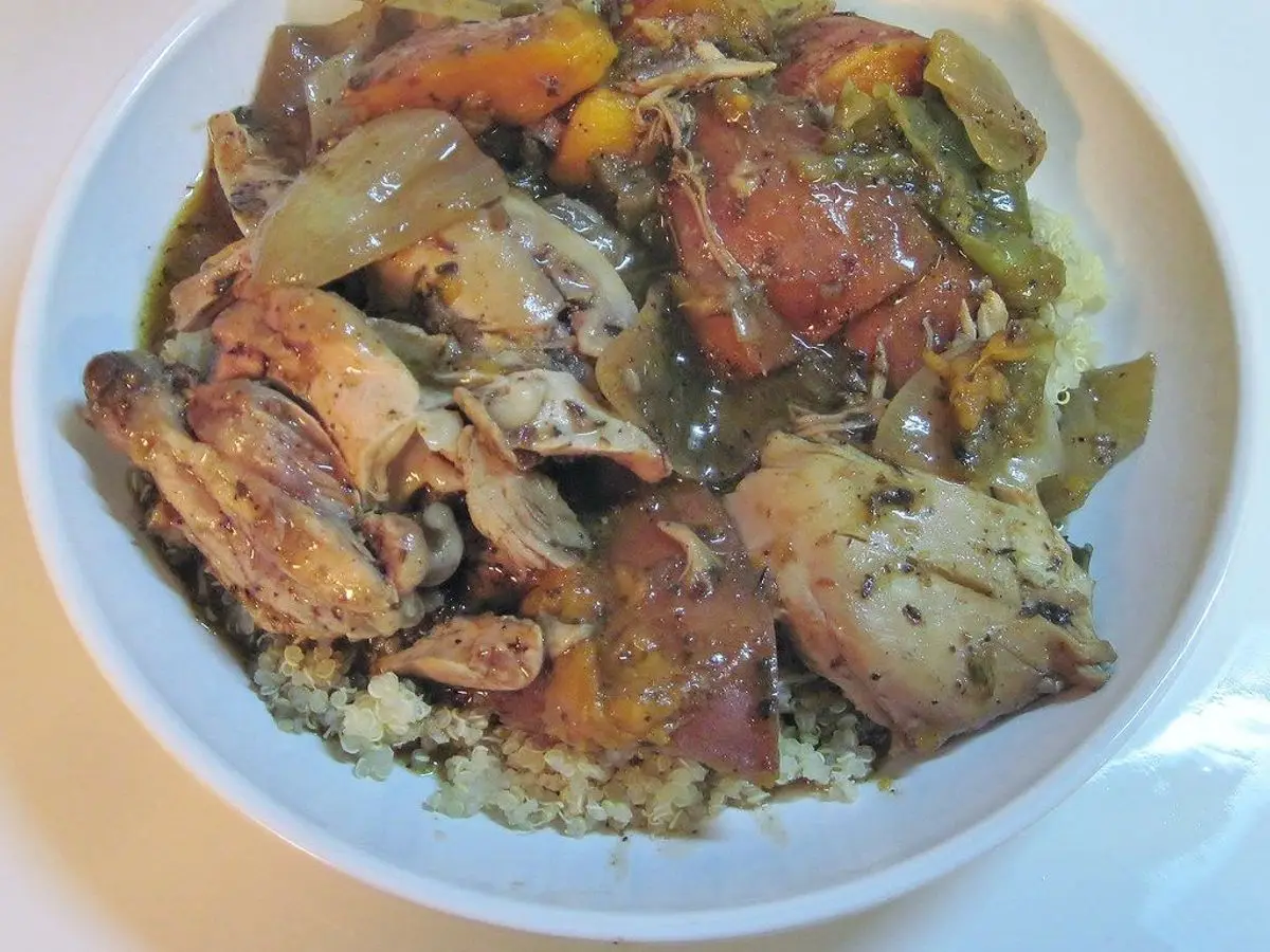 Plato blanco de pollo guisado con cebolla y verduras sobre un lecho de quinoa