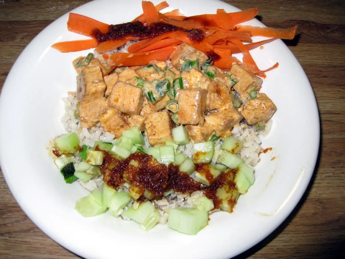 Plato de arroz con cubos de tofu dorado, pepino en rodajas, zanahoria rallada y salsa picante