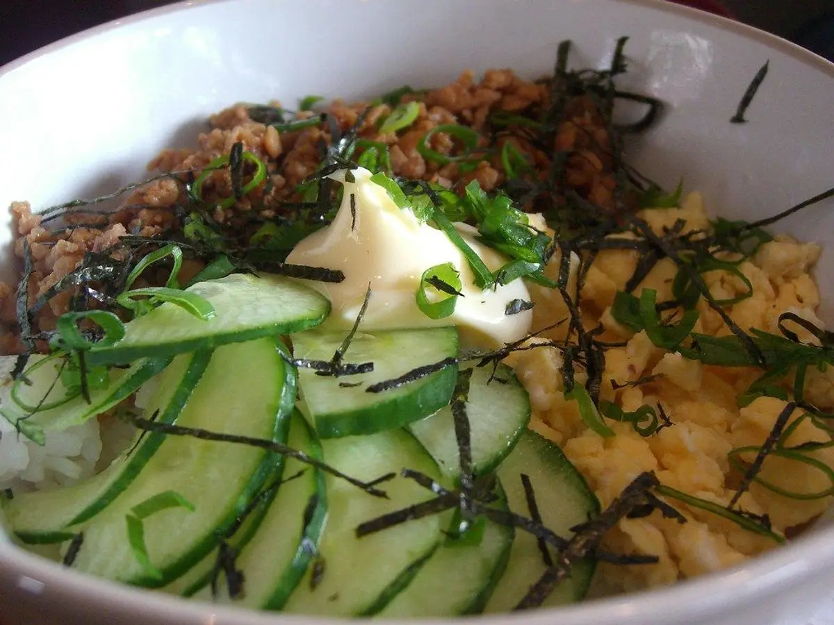 Cuenco de arroz con rodajas de pepino, huevo revuelto, tiras de alga y salsa blanca