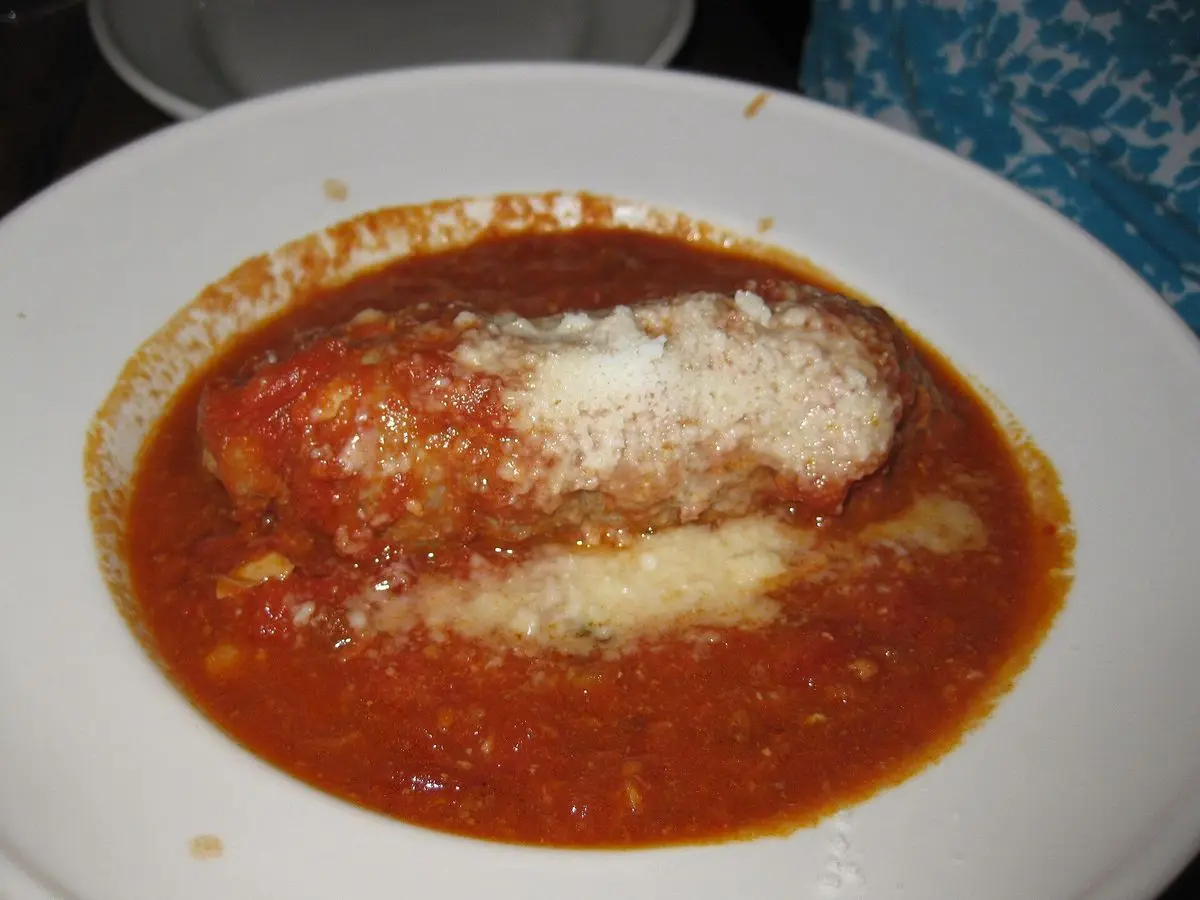 Plato blanco con rollito de carne en abundante salsa de tomate con queso rallado por encima