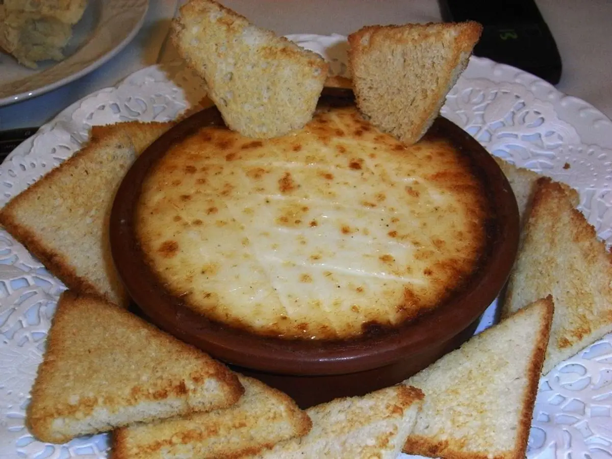 Brandada de bacalao gratinada en cazuela de barro rodeada de tostas de pan crujientes