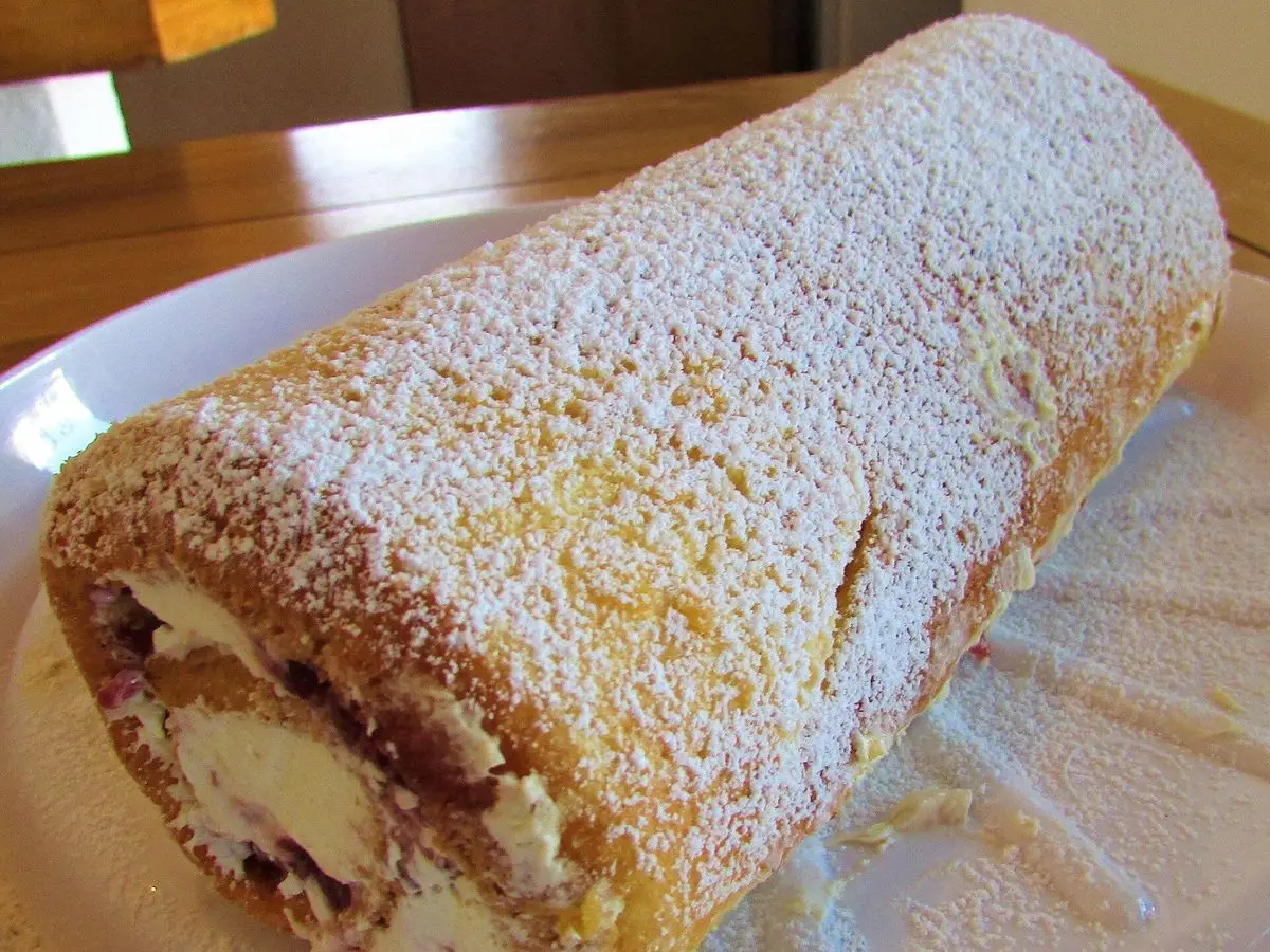 Brazo de gitano, bizcocho enrollado espolvoreado con azúcar glas y relleno cremoso, sobre un plato