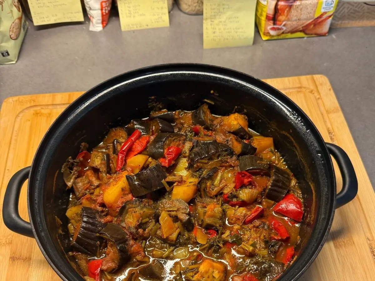 Cazuela negra de hierro con verduras al horno troceadas, berenjena, pimiento rojo y patata, sobre una tabla de madera