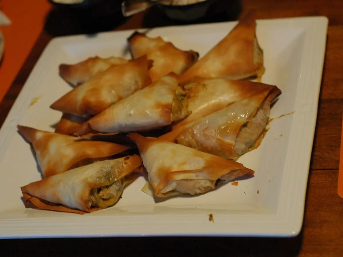 Briouats triangulares de masa filo dorada servidos en una fuente blanca