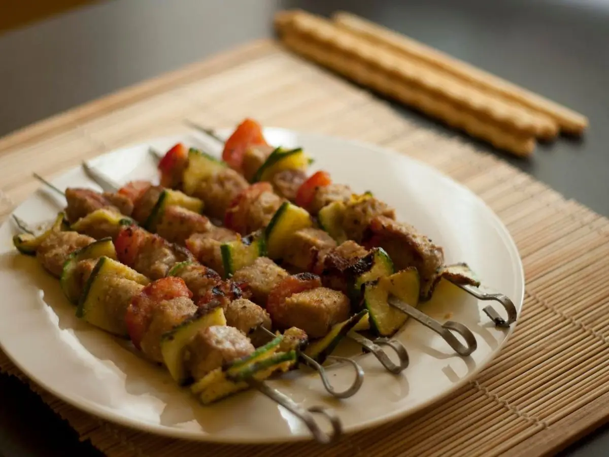 Plato con brochetas de atún, calabacín y tomate sobre un mantel de bambú con colines