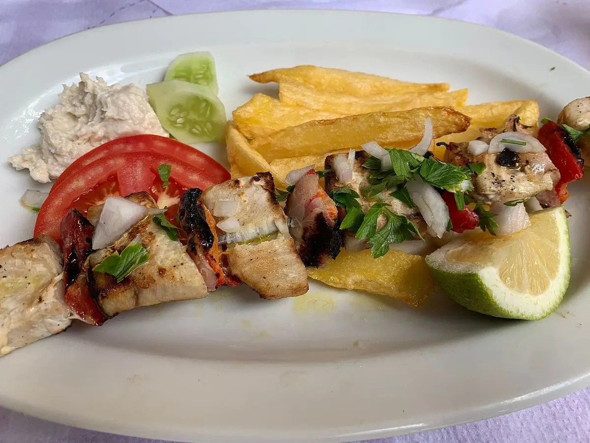 Brocheta de pescado a la parrilla con tomate, cebolla, patatas fritas y limón en un plato ovalado