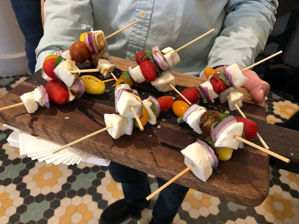 Brochetas de tomate cherry, cubos de queso blanco y pimiento sobre una tabla de madera