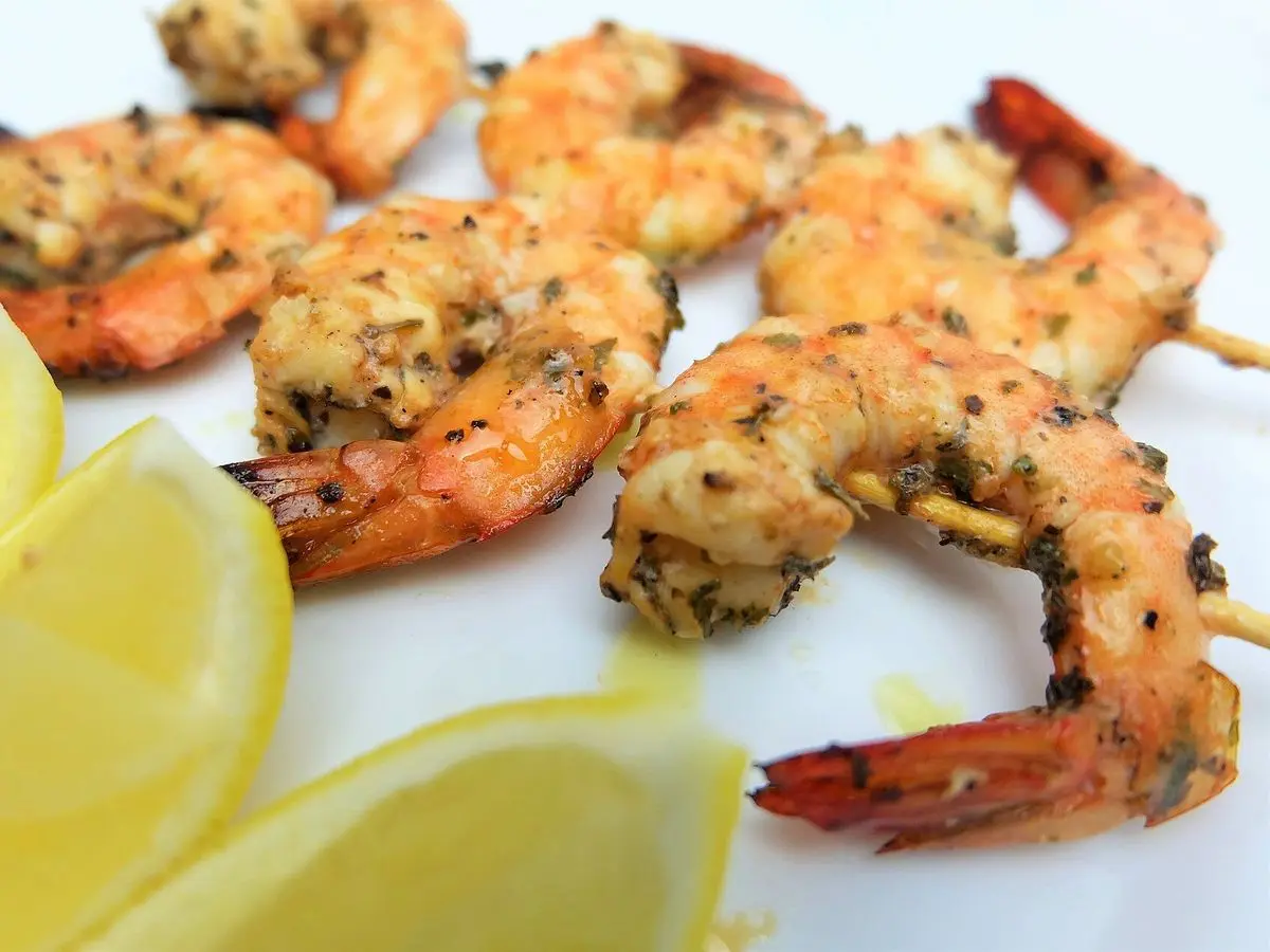 Gambas grandes a la plancha con hierbas y rodajas de limón sobre un plato blanco