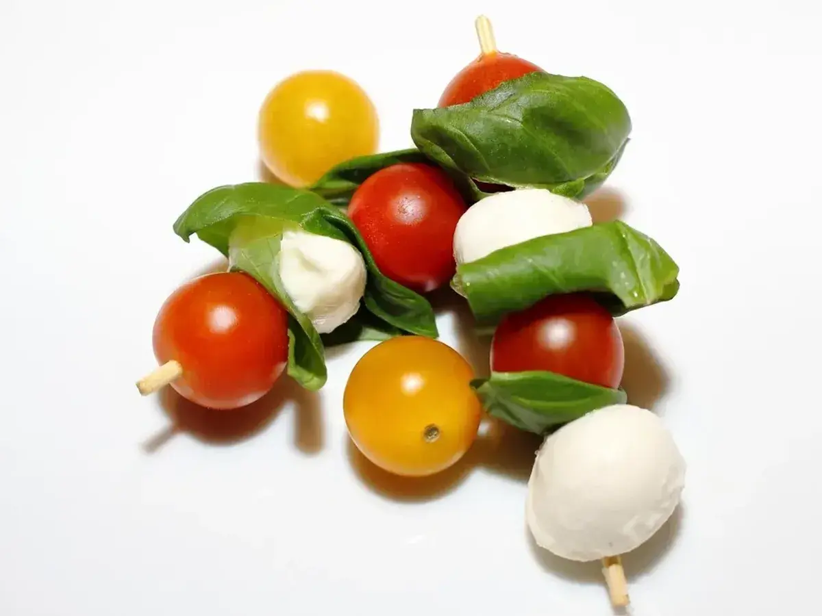 Brocheta de tomates cherry rojos y amarillos con bolas de mozzarella y albahaca sobre fondo blanco