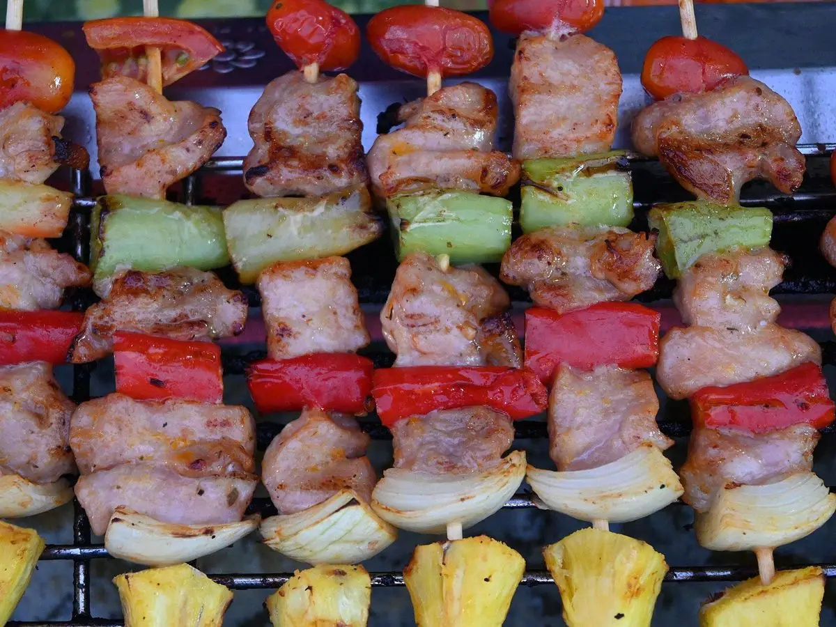 Brochetas de carne con pimiento rojo, pimiento verde, cebolla y trozos de piña en la parrilla