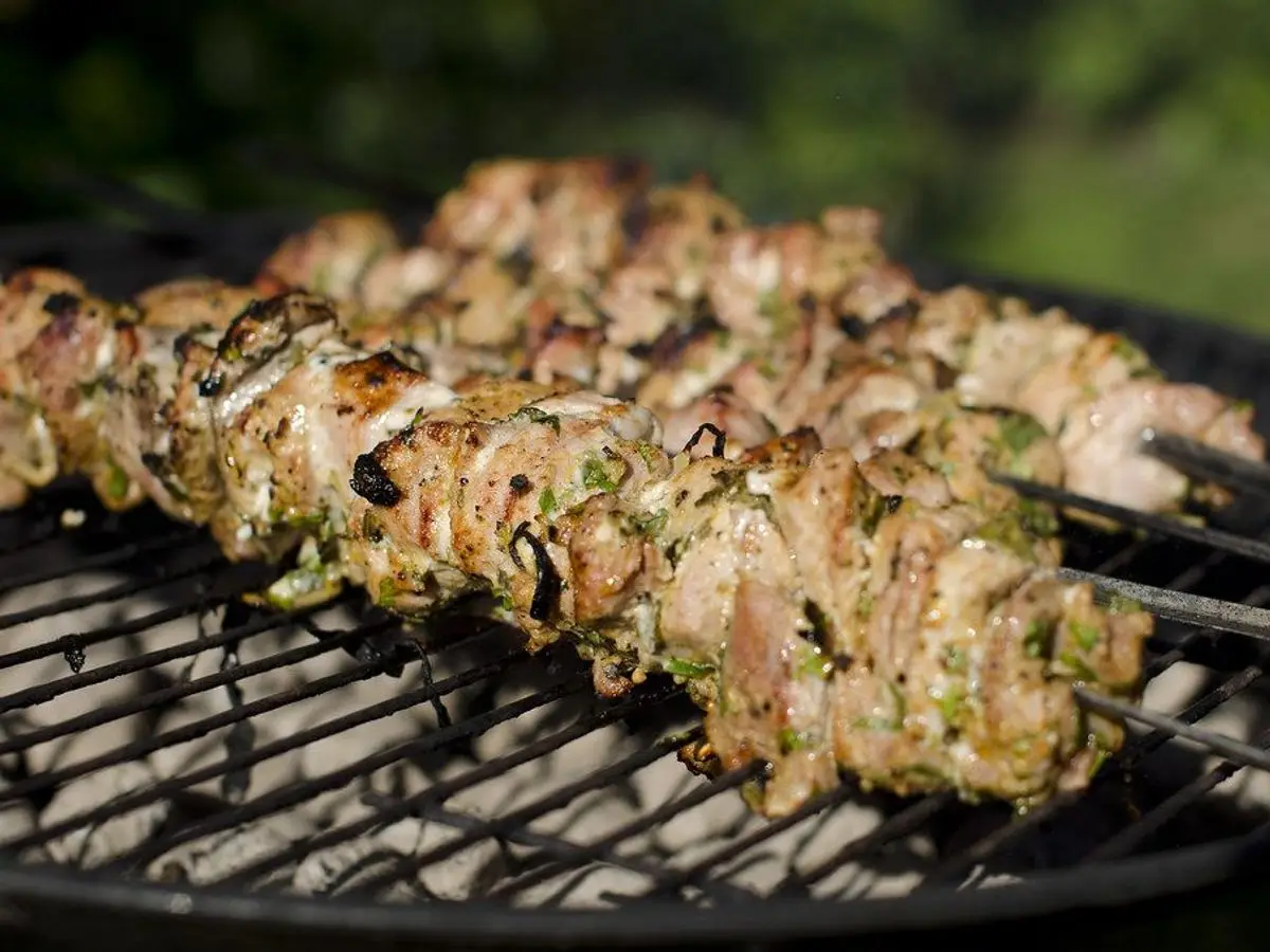 Brochetas de carne especiada asadas sobre una parrilla con hierbas