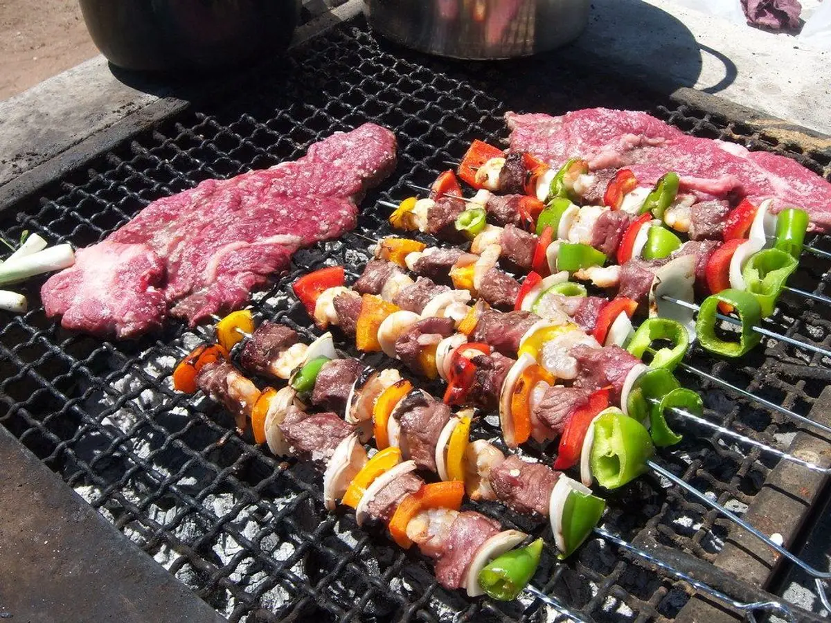 Brochetas de carne con pimientos rojos, amarillos y verdes sobre la parrilla, junto a un filete