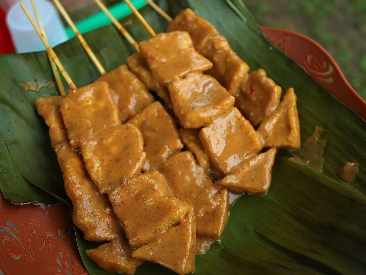 Brochetas de tofu frito dorado con salsa de cacahuete sobre una hoja de plátano