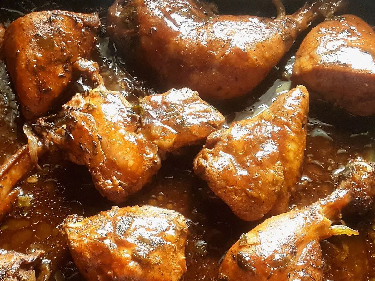 Trozos de pollo guisados en una salsa oscura y brillante con cebolla, vistos de cerca