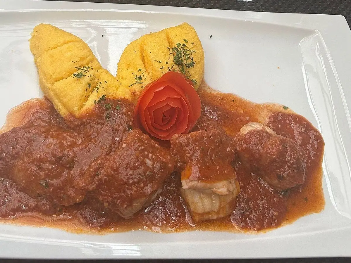 Plato blanco con pescado guisado en salsa de tomate oscura y dos porciones de polenta amarilla