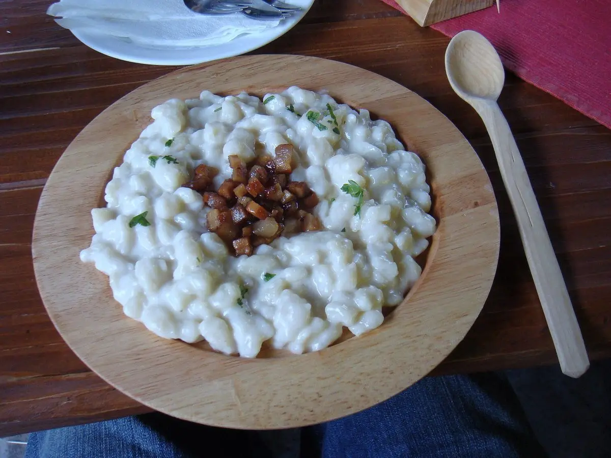 Ñoquis pequeños con queso cremoso y trozos de bacon en un plato de madera con cuchara