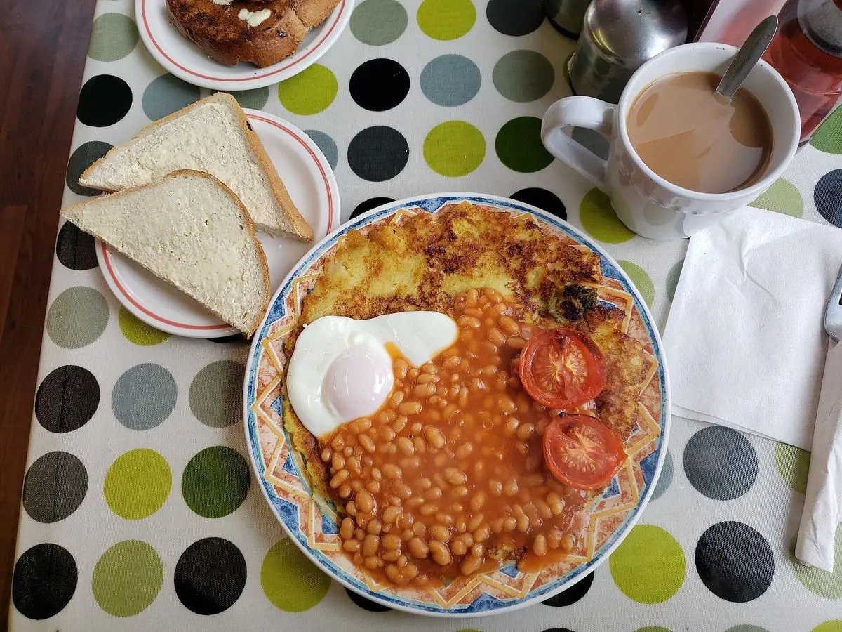 Plato de desayuno con tortita dorada de patata y col, huevo frito, alubias en salsa de tomate y tomates asados