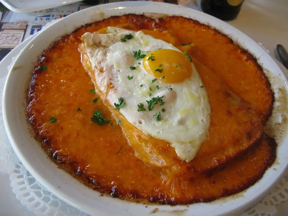 Tostada de queso fundido gratinado con huevo frito y hierbas en un plato blanco