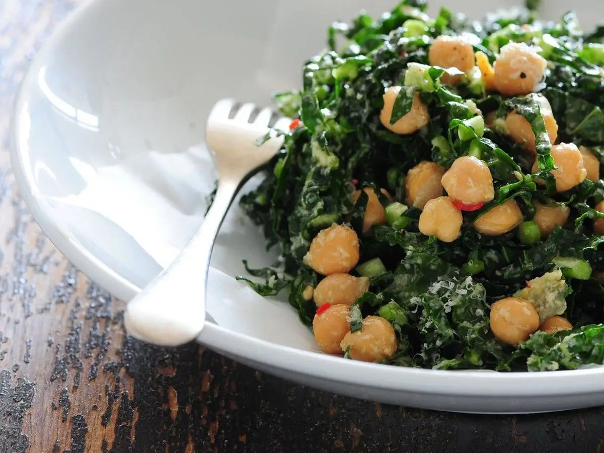 Plato blanco con garbanzos y hojas de kale troceadas, con un tenedor al lado