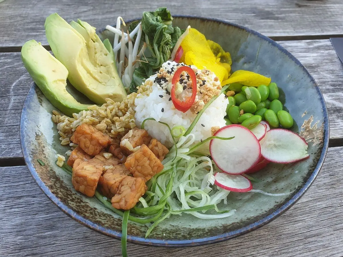 Buddha bowl con cubos de proteína dorada, aguacate, rabanitos, edamame y brotes
