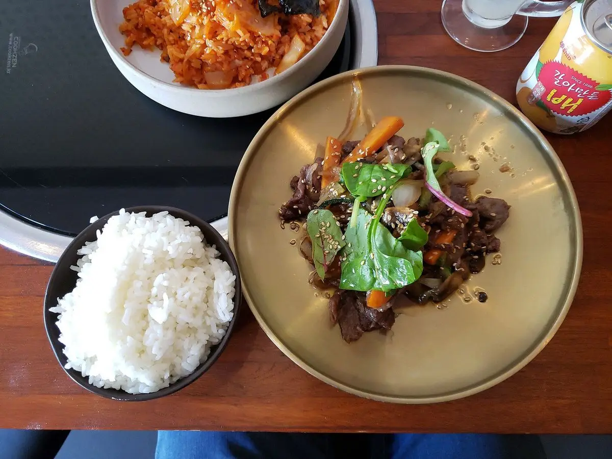 Plato de bulgogi de ternera con hojas verdes y cebolla junto a un cuenco de arroz blanco