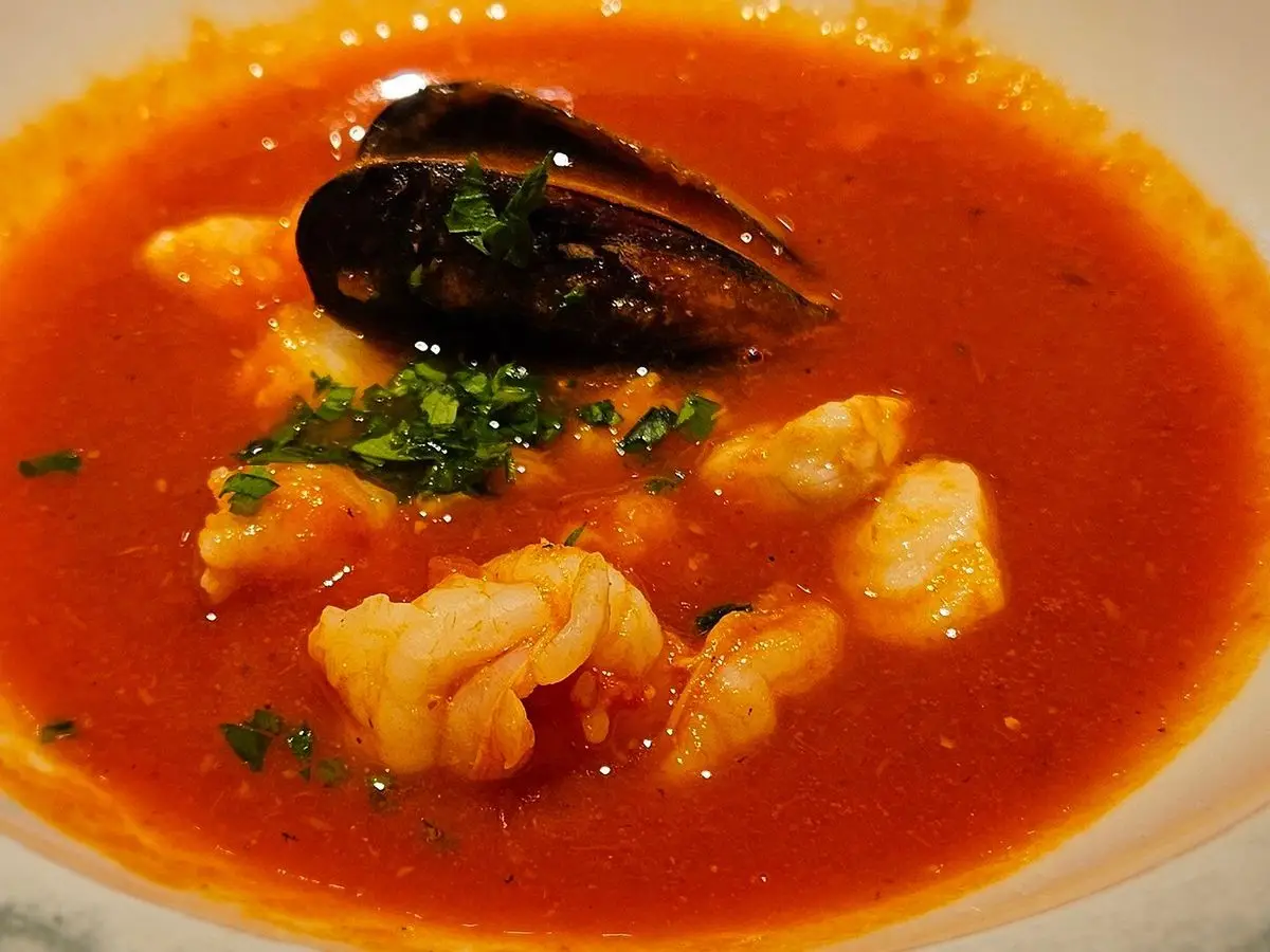 Plato hondo de sopa de pescado de tomate con un mejillón, trozos de pescado y perejil